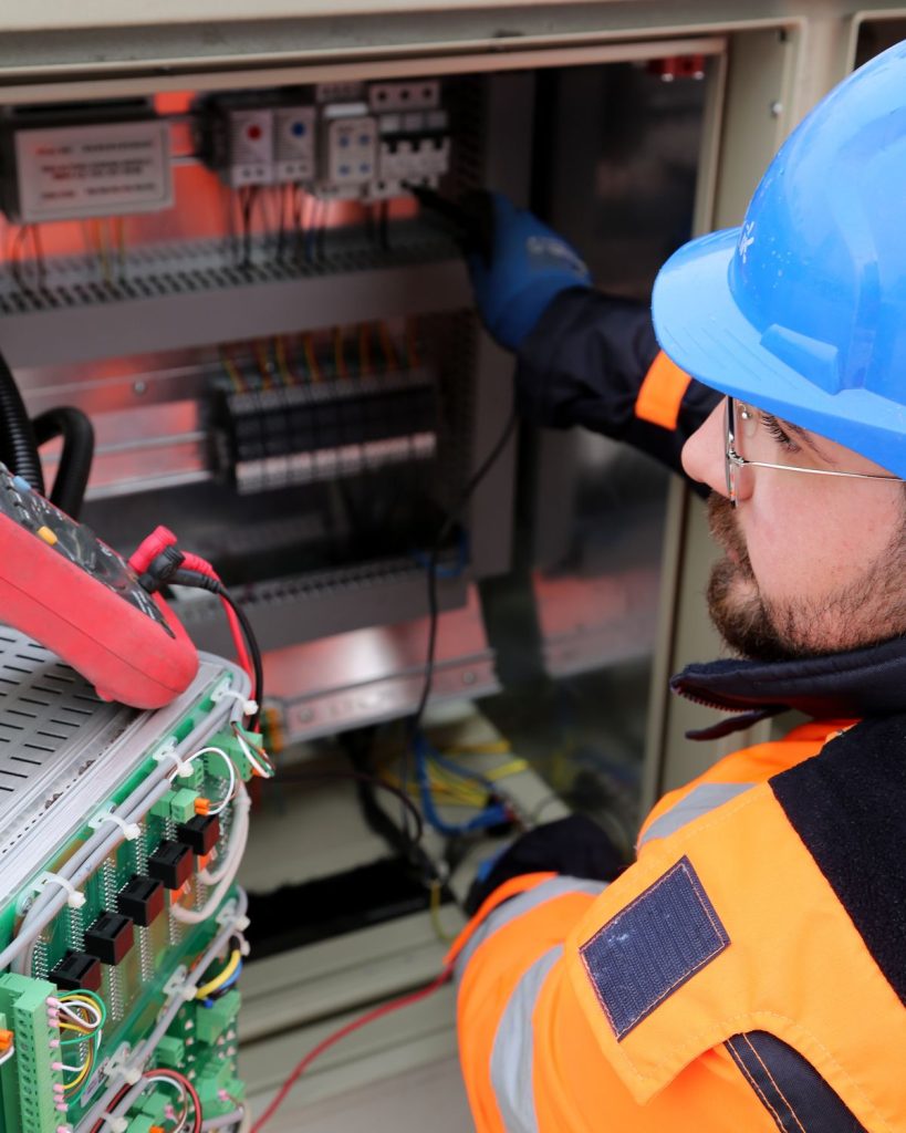 Elektriker mit Schutzhelm bei der Arbeit an einer Schaltanlage – Absicherung der Arbeitskraft